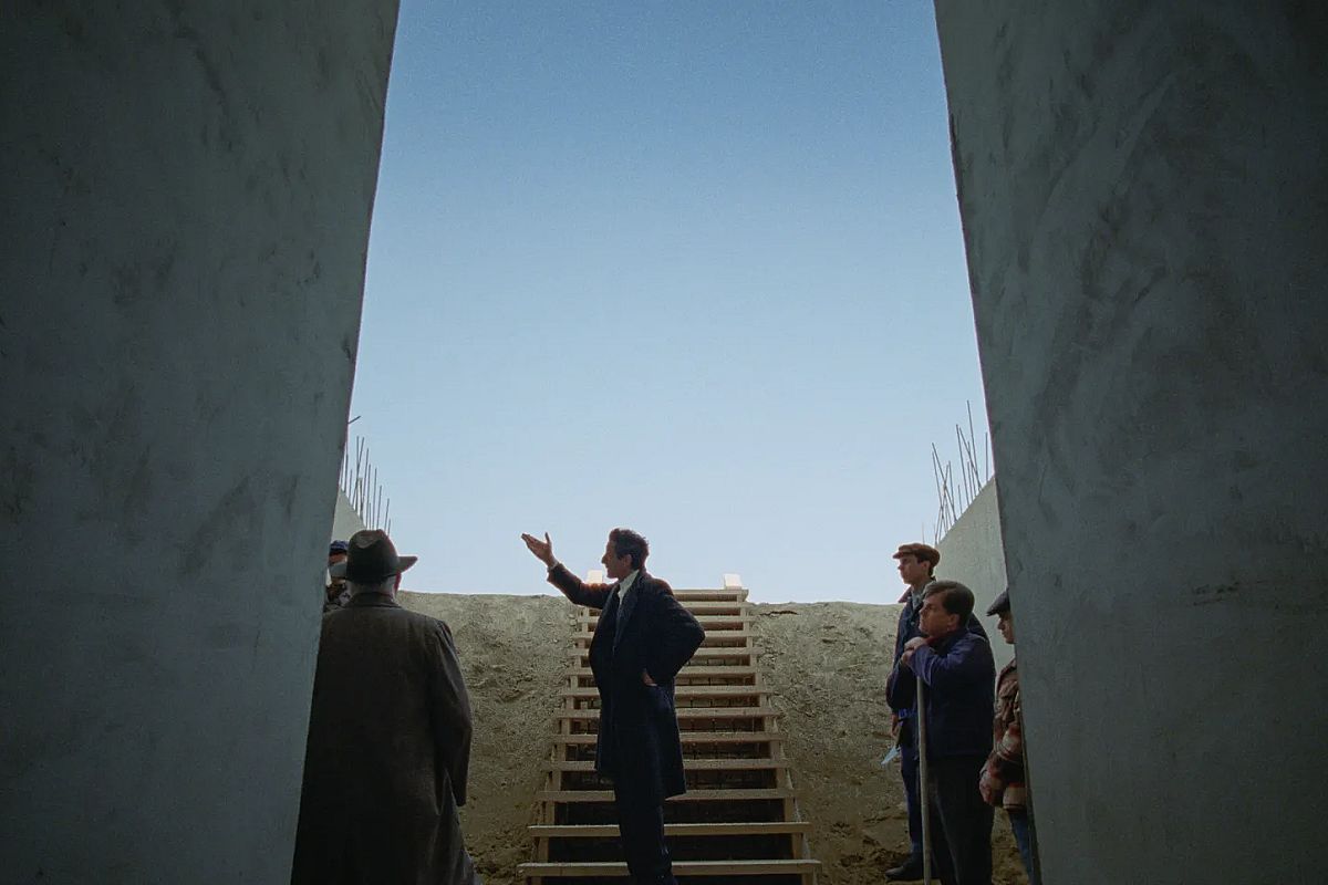 Still from the Brutalist film - Adrian Brody, flanked by concrete columns on both sides gestures to the left.