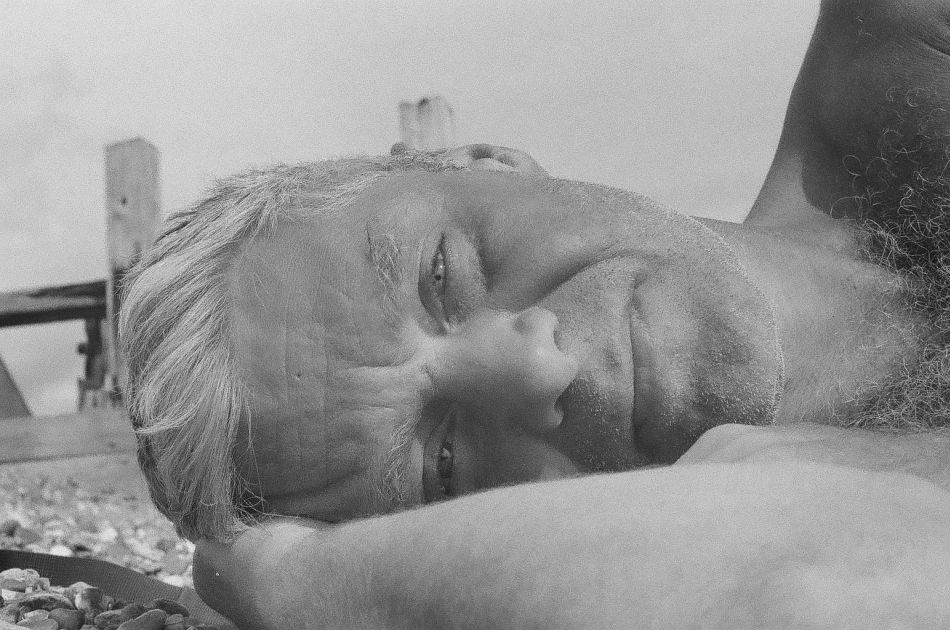 Tom Fogg, in B&W lying on the beach in a photo taken by his son.